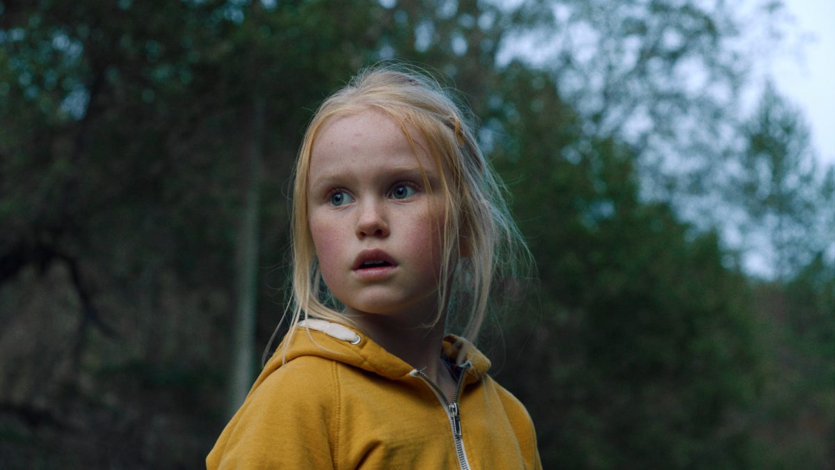 'Les Innocents' Rakel Lenora Fløttum dans le rôle d'Ida portant une veste jaune regardant devant avec des arbres en arrière-plan