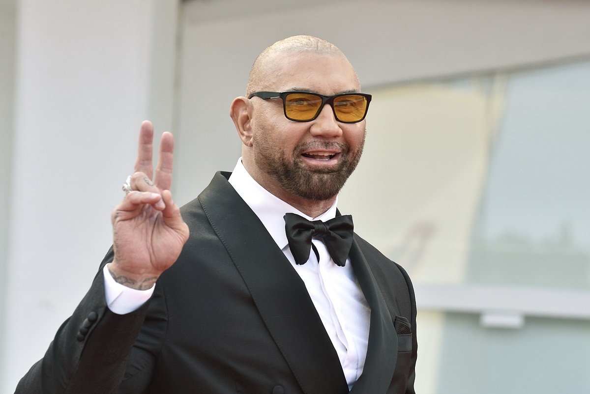 Dave Bautista souriant tout en portant un costume et des lunettes de soleil.
