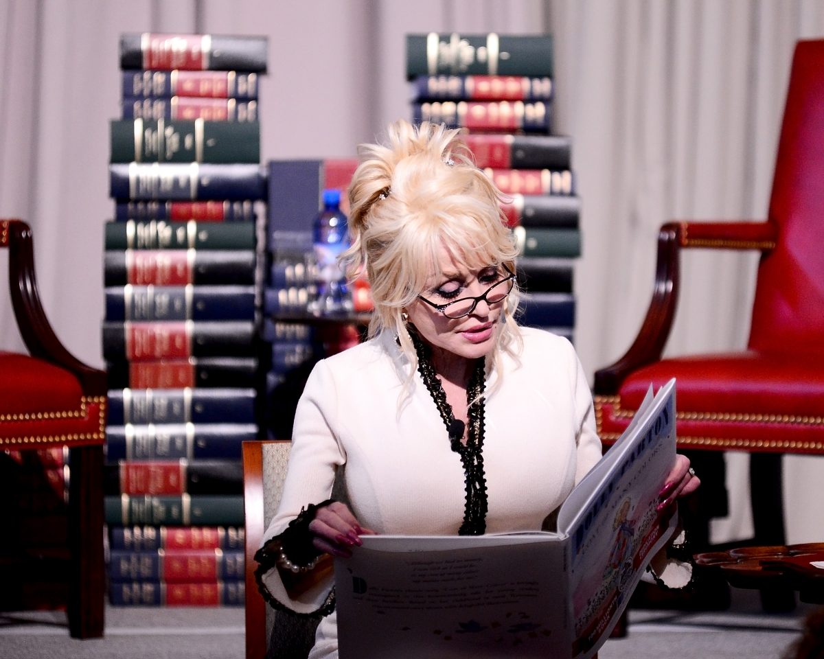 Dolly Parton est assise devant des piles de livres et lit un livre pour enfants.