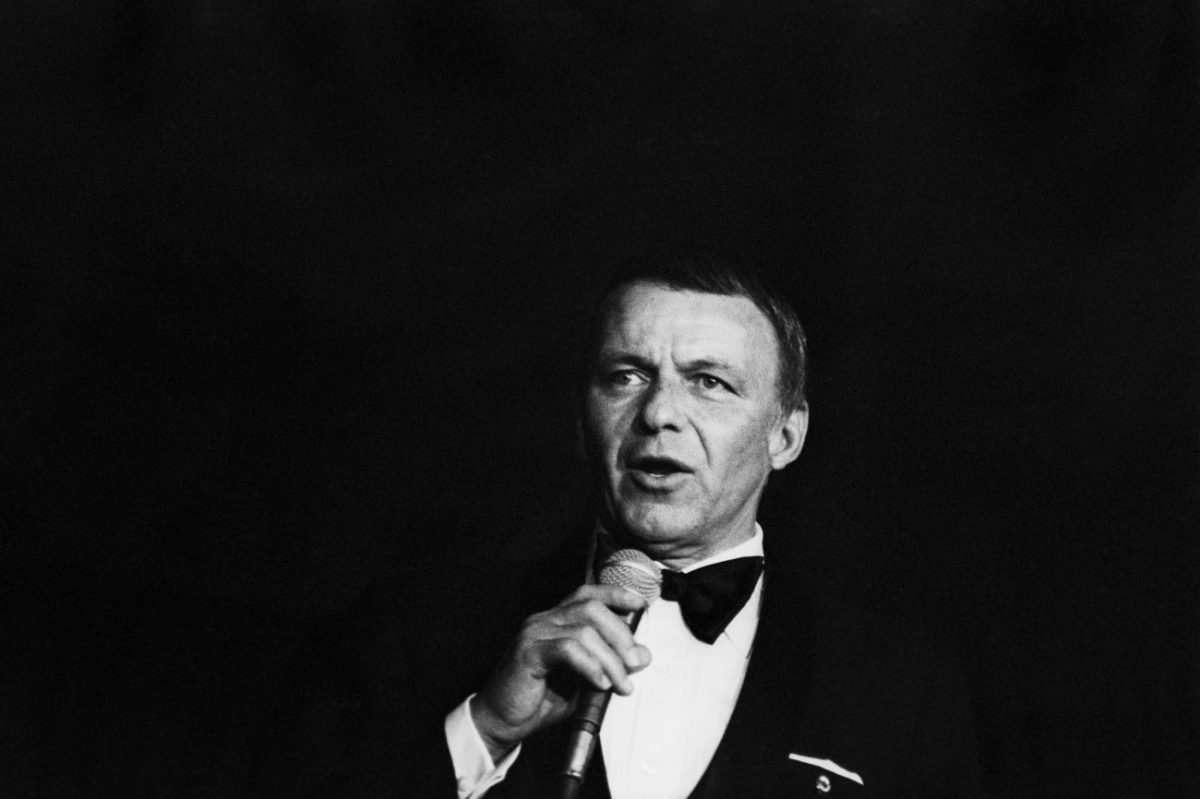 Une photo en noir et blanc de Frank Sinatra portant un smoking et tenant un microphone.
