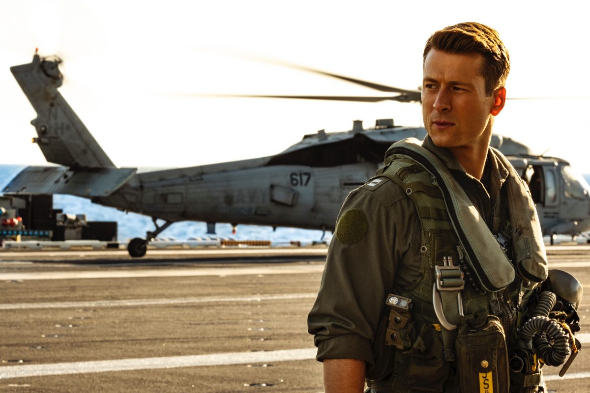 'Top Gun: Maverick' Glen Powell en tant que pendu portant un uniforme devant un hélicoptère