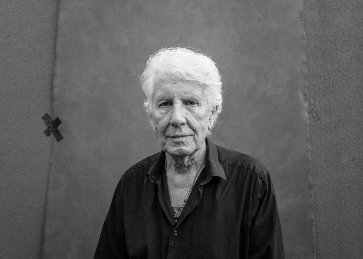 Graham Nash photographié en noir et blanc contre un mur.