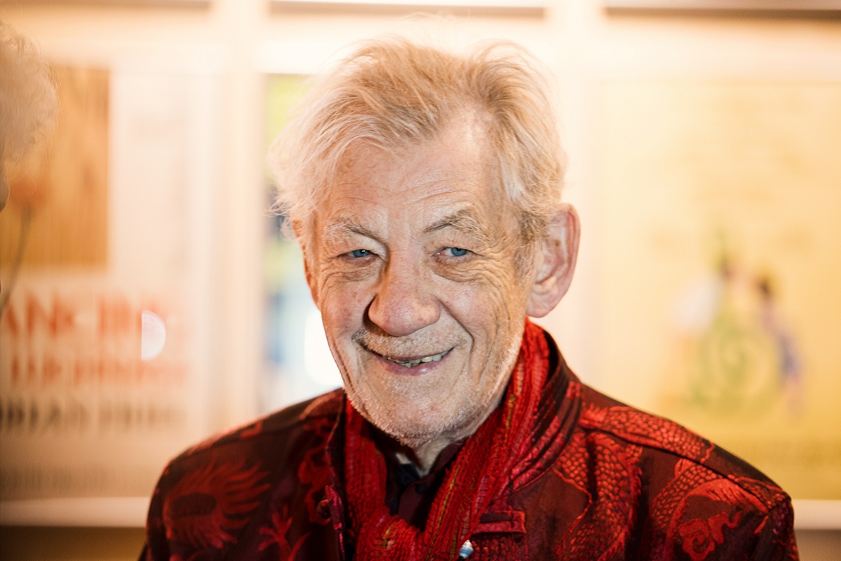 Ian McKellen souriant tout en portant une veste rouge.