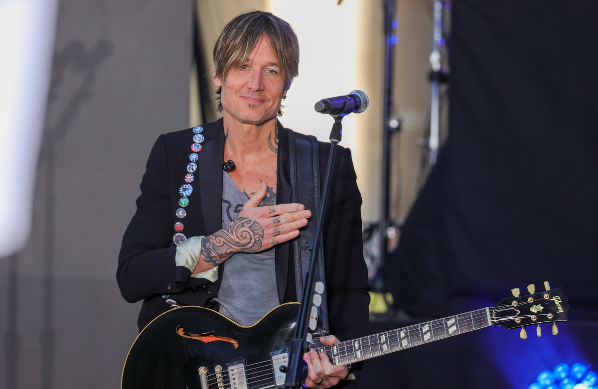 Keith Urban tient sa guitare sur scène avec une main sur son cœur tout en souriant.