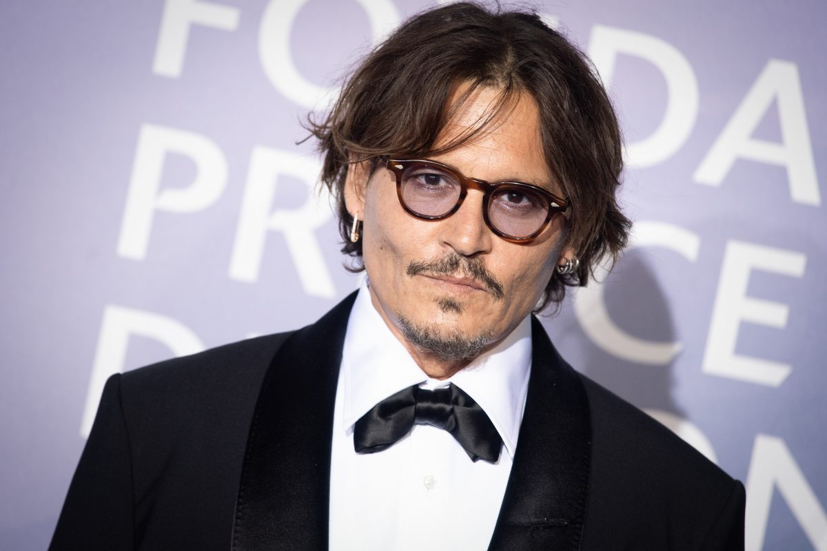 Johnny Depp pose lors d'un événement tout en portant un costume noir et une chemise blanche.