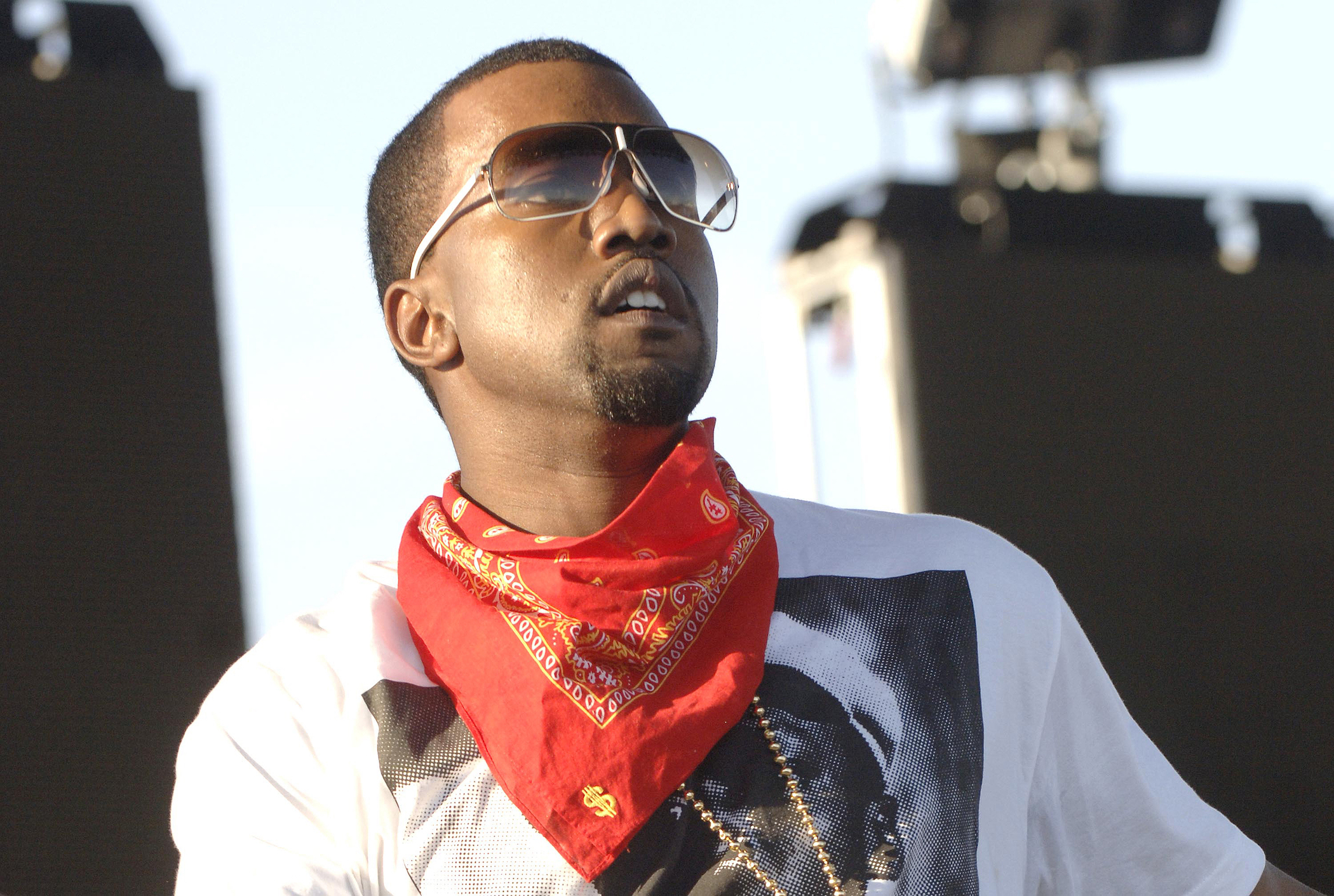Un gros plan de Kanye West portant des lunettes de soleil et un bandana rouge autour du cou