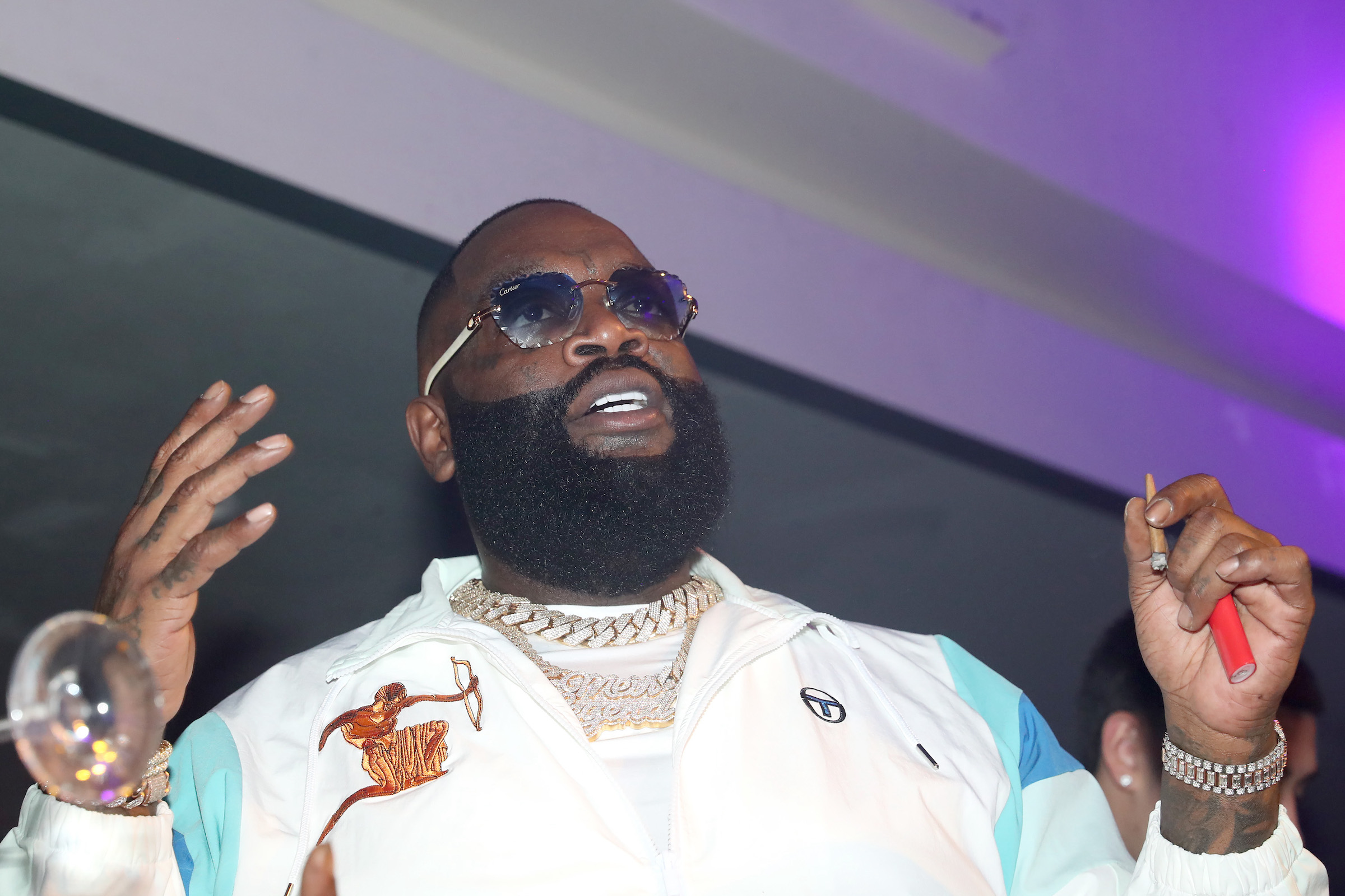 Le collectionneur de voitures Rick Ross portant une veste blanche et fumant