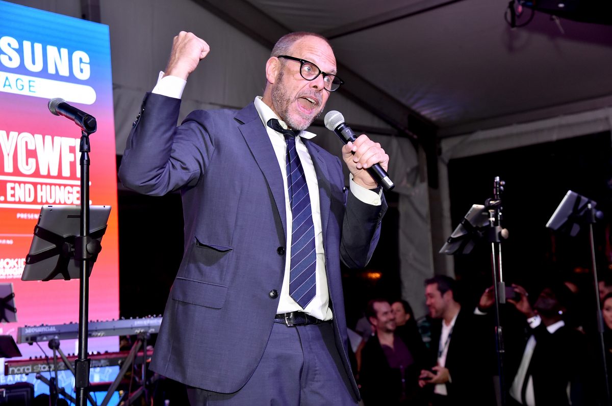 La personnalité culinaire Alton Brown porte un costume et une cravate sur scène lors d'un événement Food Network sur cette photo.