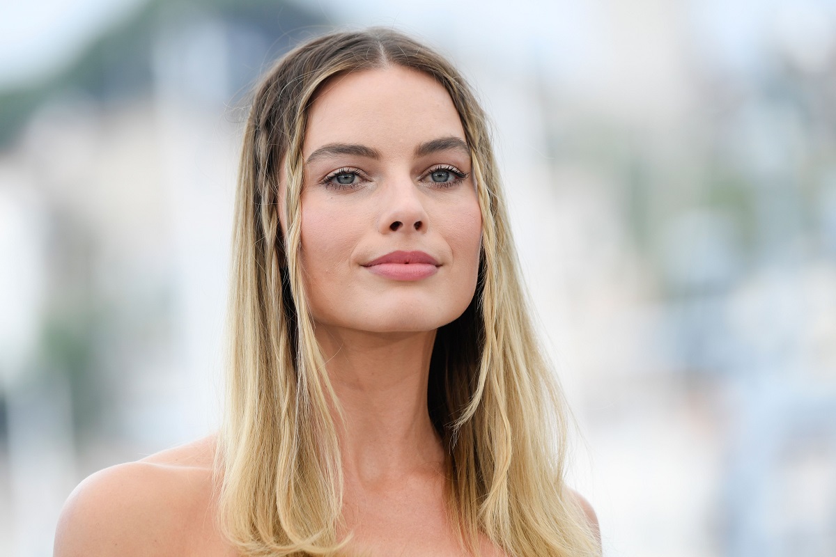 Margot Robbie sourit en portant une robe blanche.