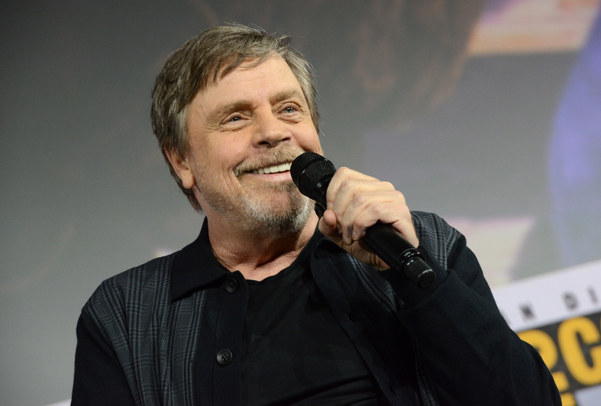 Mark Hamill souriant tout en tenant un microphone.