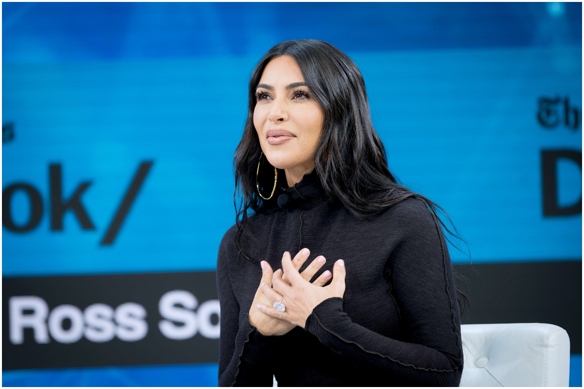 Kim Kardashian West assise et souriante avec ses mains sur sa poitrine.