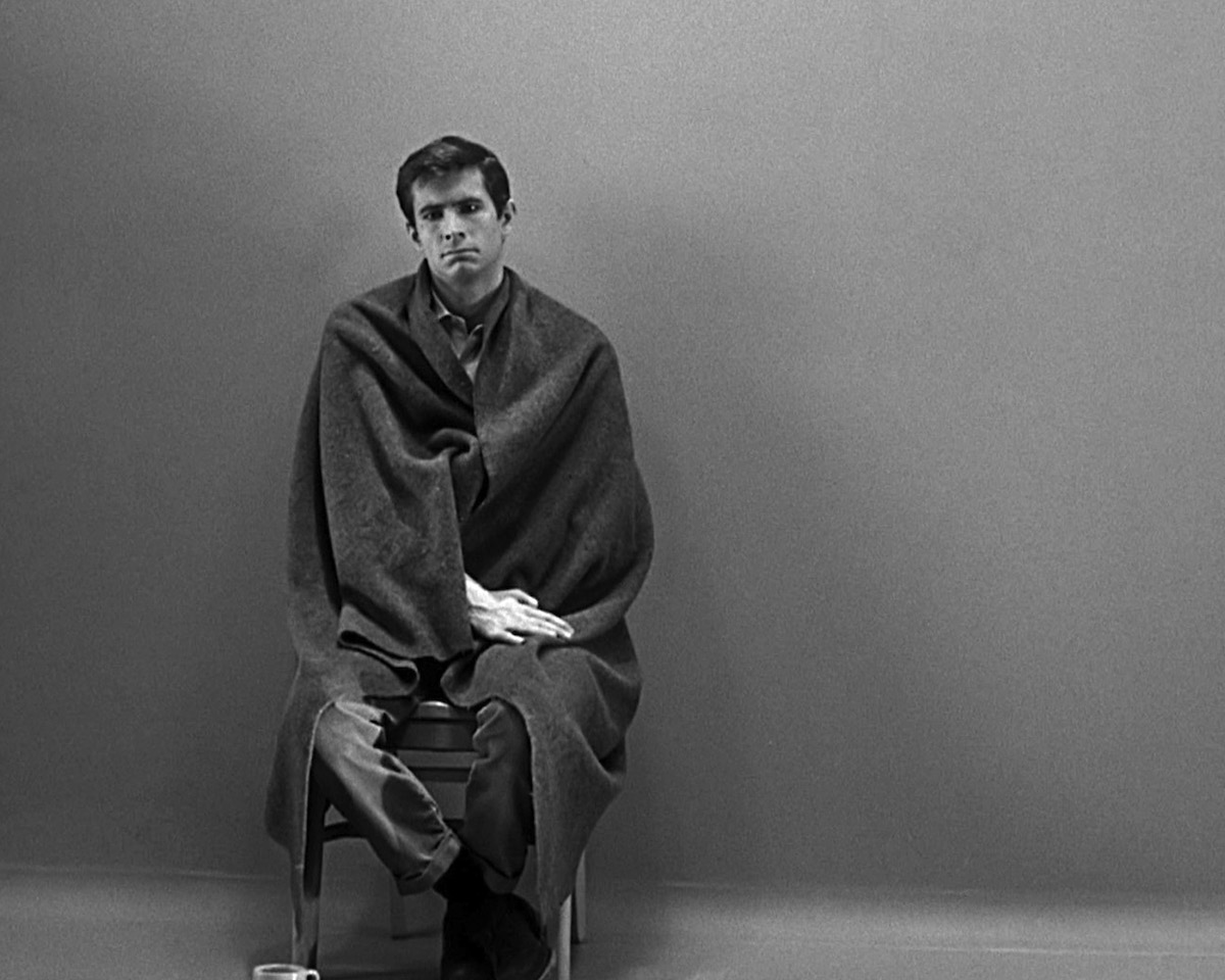 Anthony Perkins dans le rôle de Norman Bates assis, en noir et blanc