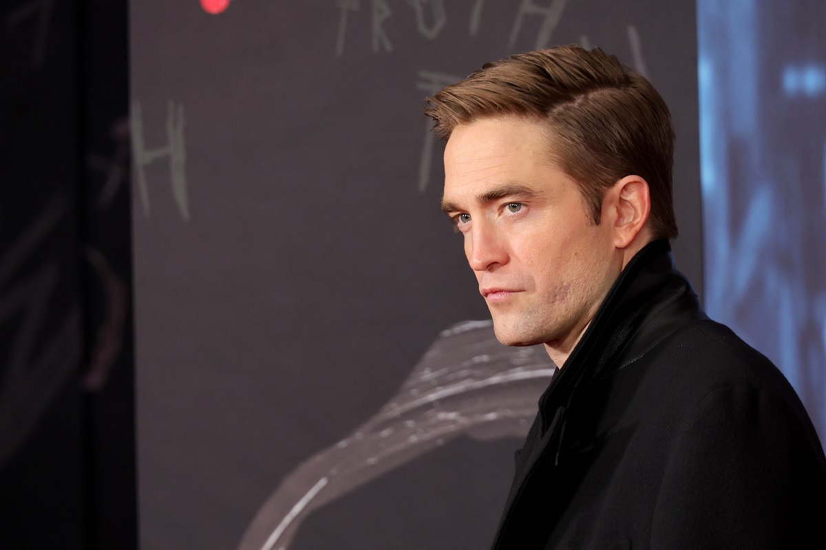 Robert Pattinson posant en portant un trench-coat noir et un costume.