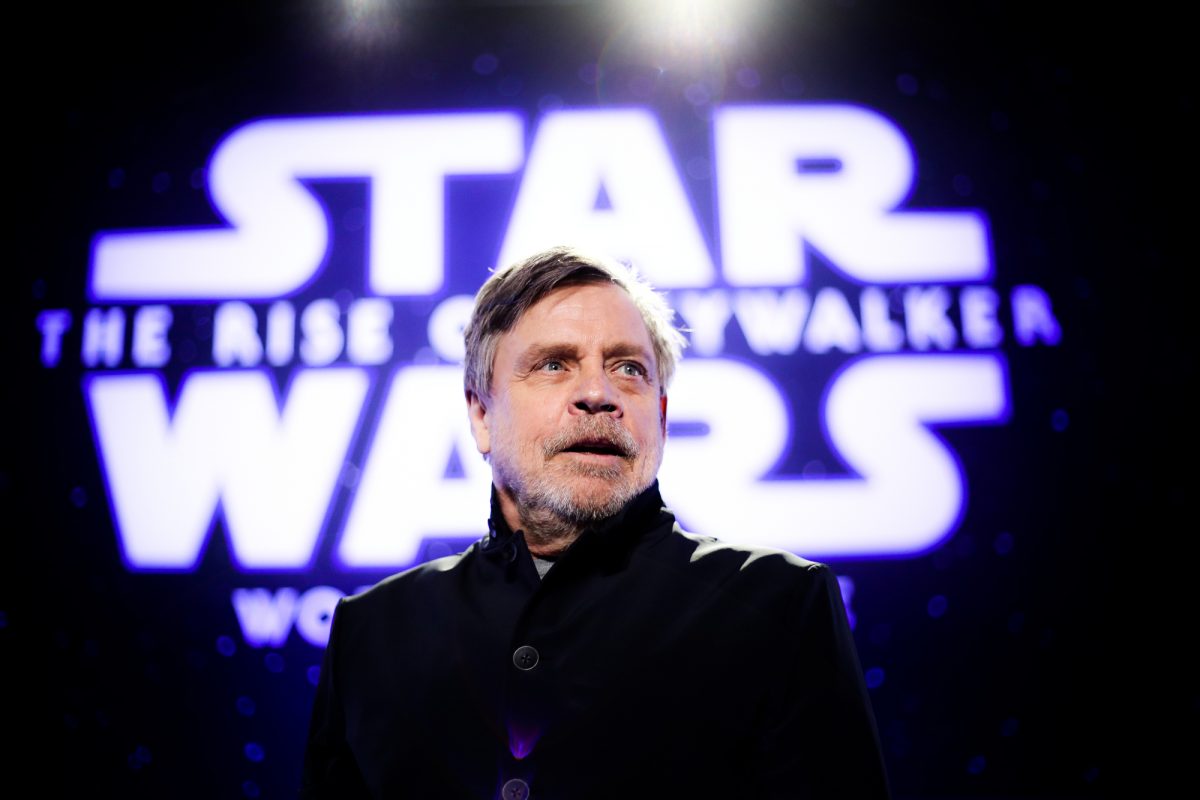 L'acteur de 'Star Wars' Mark Hamill debout devant le logo illuminé portant un manteau noir