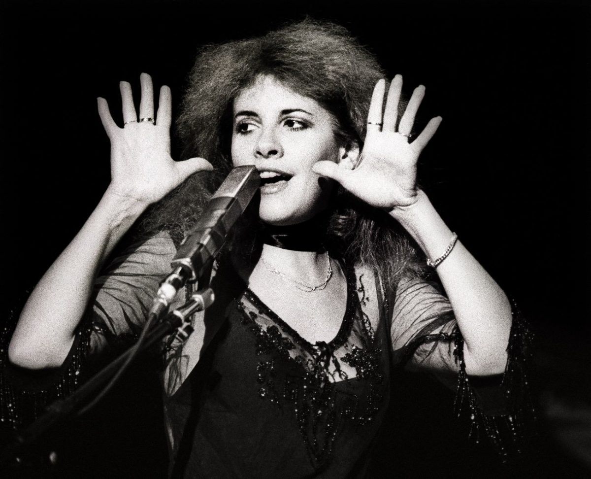 Une photo en noir et blanc de Stevie Nicks vêtue d'une robe transparente et debout devant un microphone.