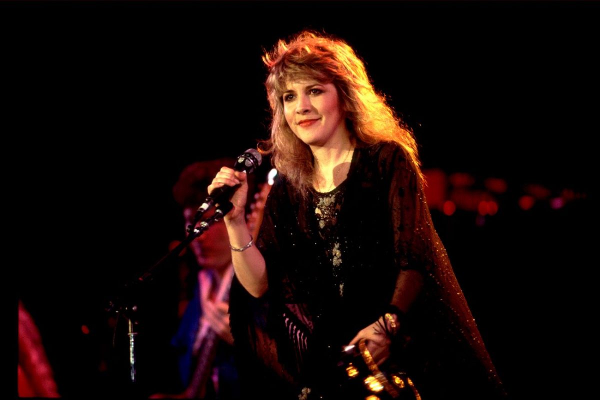 Stevie Nicks porte une tenue noire et se tient sur scène avec un microphone.