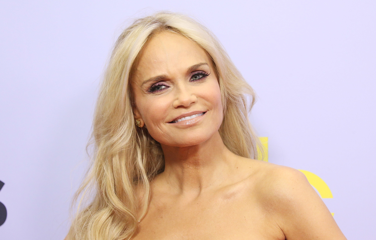 Kristin Chenoweth sourit devant un fond violet.