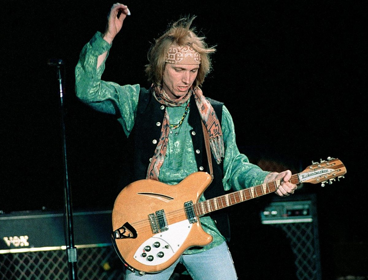 Le musicien américain Tom Petty porte une chemise et un gilet verts et gratte la guitare.