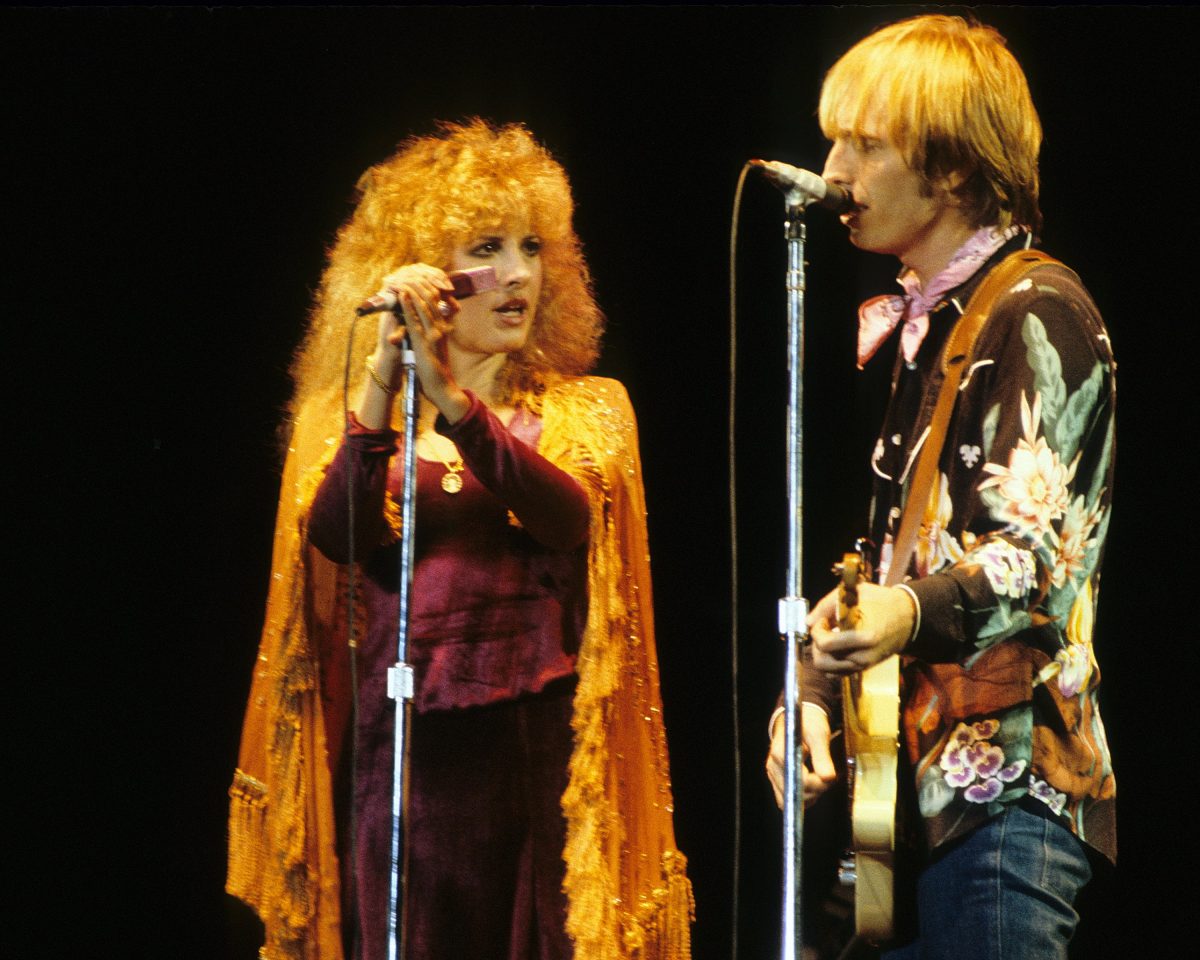 Stevie Nicks et Tom Petty chantent tous les deux dans des microphones. Tom Petty tient une guitare.