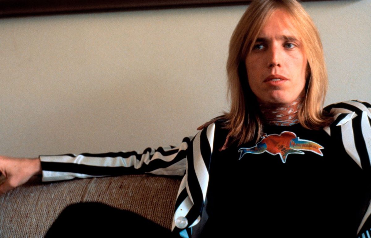 Tom Petty porte une veste à rayures noires et blanches et est assis sur un canapé.