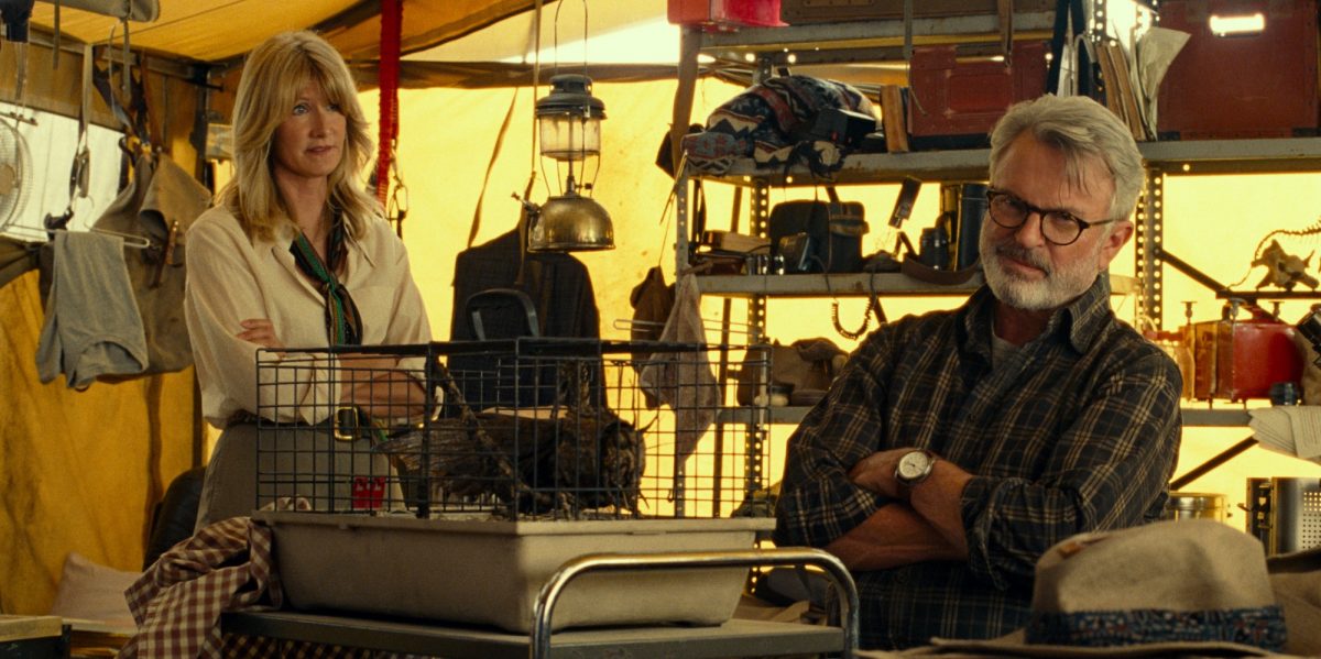 'Jurassic World Dominion' Laura Dern dans le rôle du Dr Ellie Sattler et Sam Neill dans le rôle du Dr Alan Grant dans une tente entourée d'objets du site de fouilles, les bras croisés.