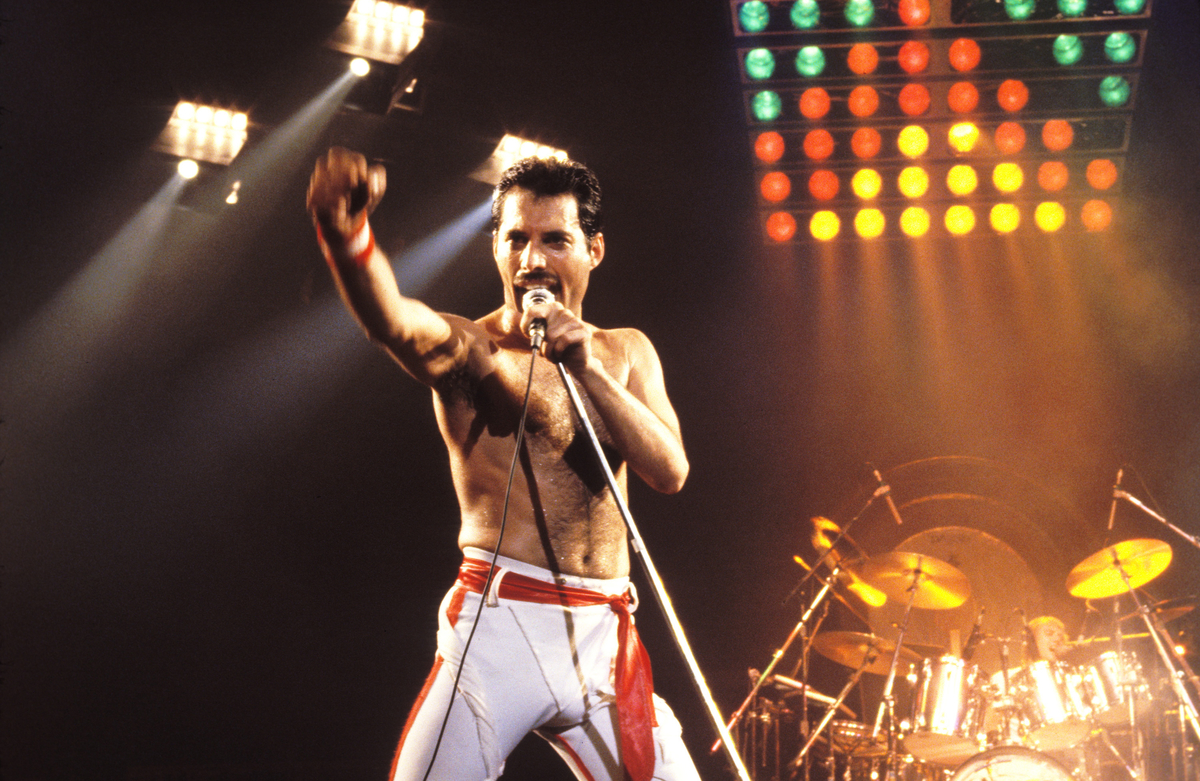 Freddie Mercury de Queen fait un poing sur scène alors qu'il chante dans un microphone.
