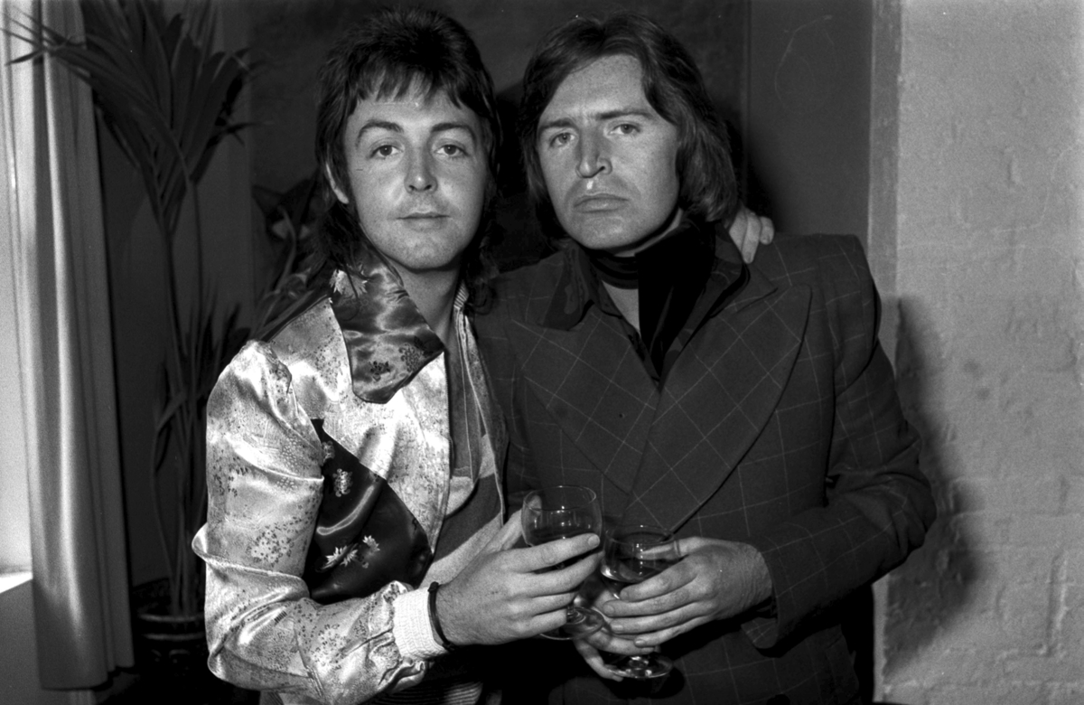 Paul McCartney et son frère Mike tiennent des verres à vin et se tiennent côte à côte en souriant.