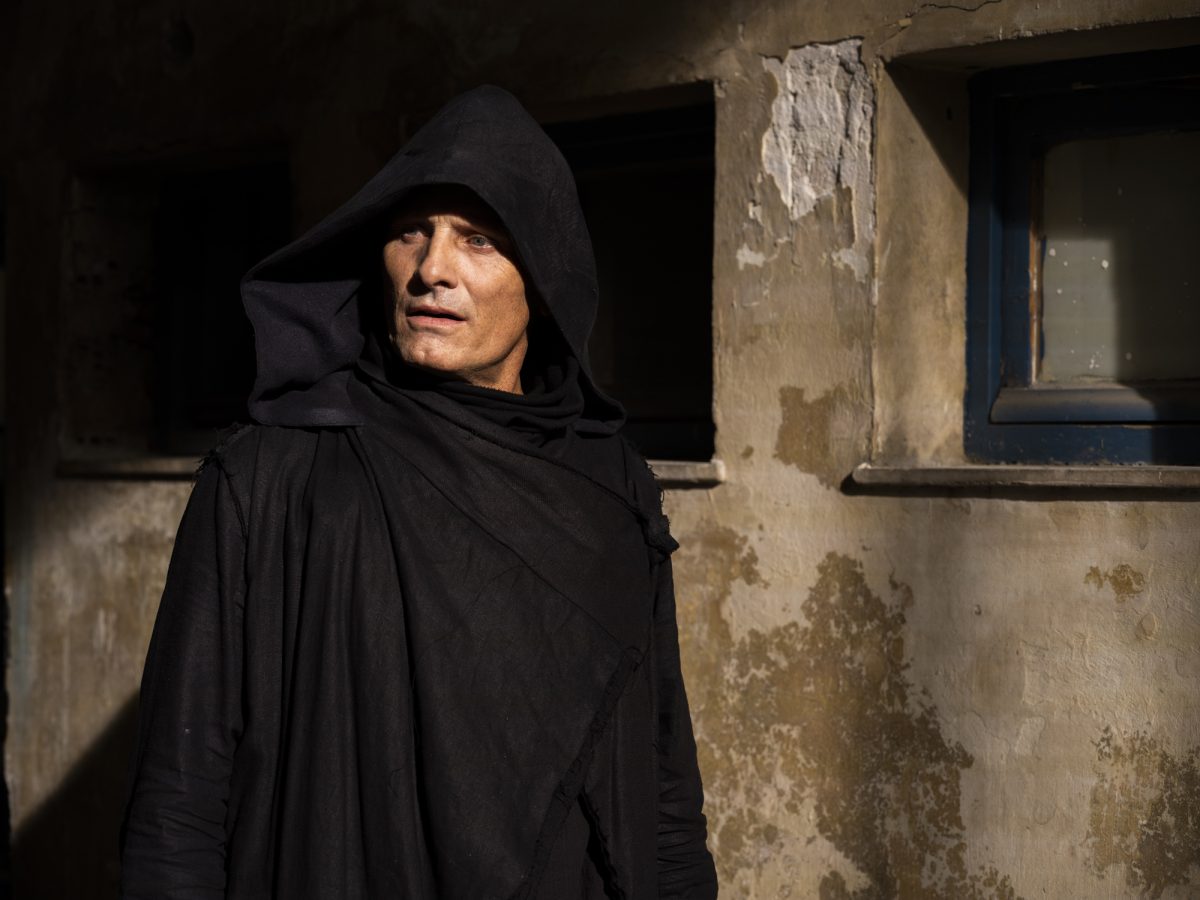 'Crimes of the Future' Viggo Mortensen dans le rôle de Saul Tenser vêtu de noir et d'une cagoule, marchant près d'un bâtiment