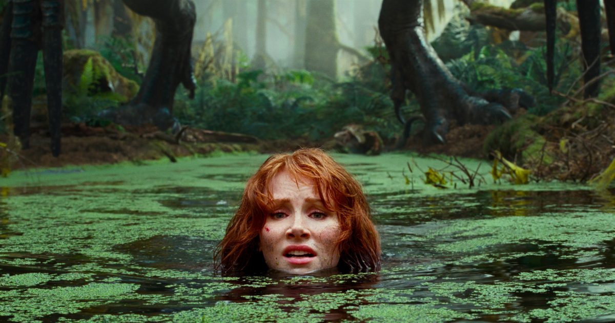 'Jurassic World Dominion' Bryce Dallas Howard dans le rôle de Claire Dearing avec la tête hors de l'eau avec de la mousse à la surface. Une paire de pattes de dinosaure se tient derrière elle sur le terrain.