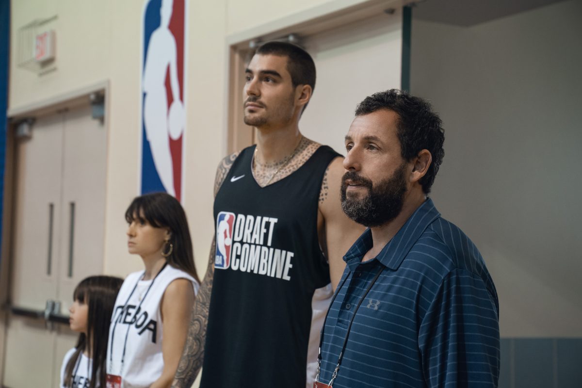 'Hustle' Ainhoa Pillet dans le rôle de Lucia, Maria Botto dans le rôle de Paola, Juancho Hernangomez dans le rôle de Bo Cruz et Adam Sandler devant le logo de la NBA regardant le terrain.