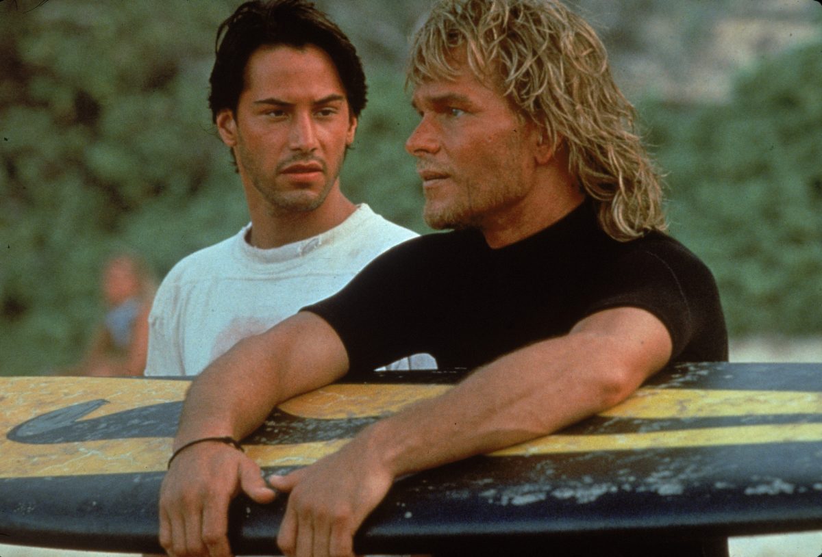 Patrick Swayze tient une planche de surf sur la plage avec Keanu Reeves et aurait fait 'Point Break 2'