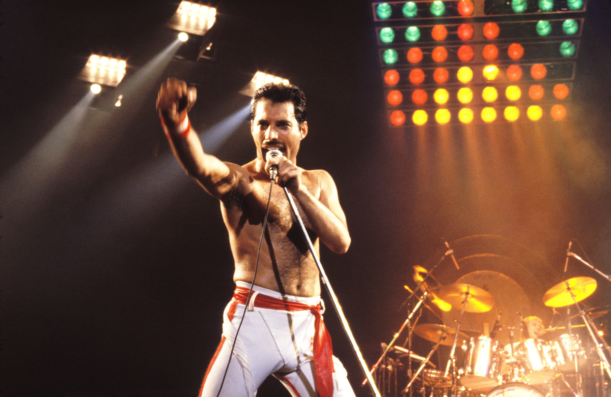Freddie Mercury de Queen se tient devant une scène éclairée de couleurs vives et chante dans un microphone