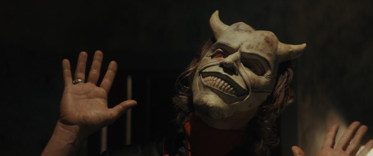 Ethan Hawke dans le rôle de The Grabber dans The Black Phone, réalisé par Scott Derrickson.  levant les yeux portant un masque de démon avec ses mains ouvertes levées