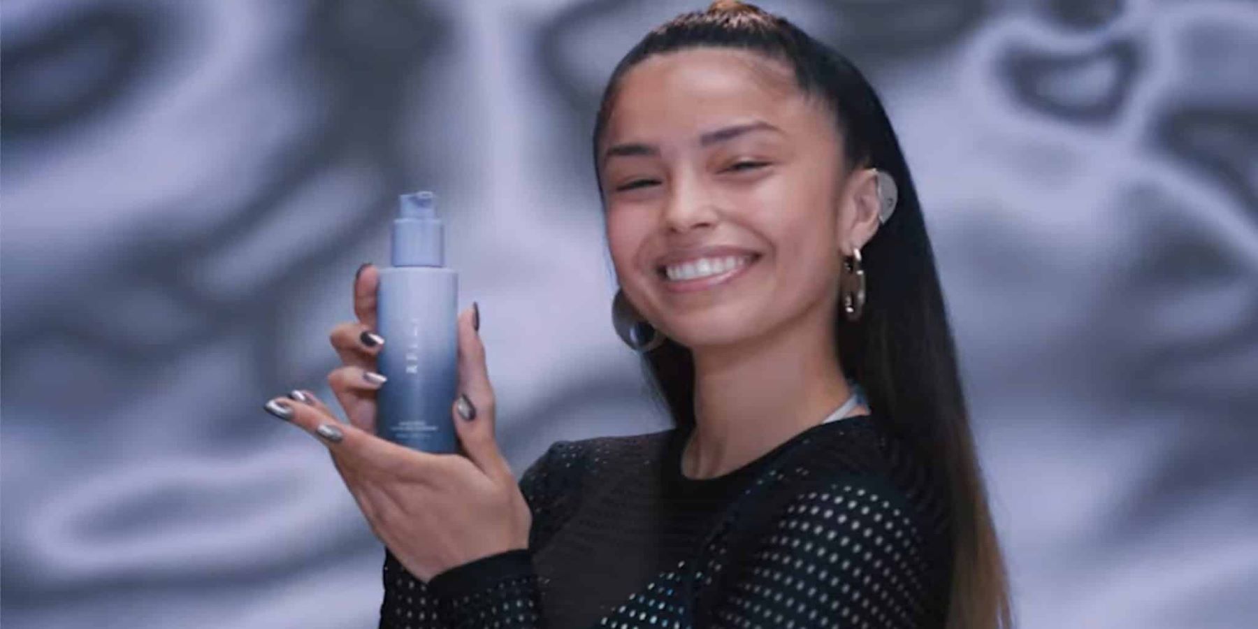 Streamer YouTube Valkyrae tenant une bouteille de produit de soin de la peau RFLCT dans une image promotionnelle
