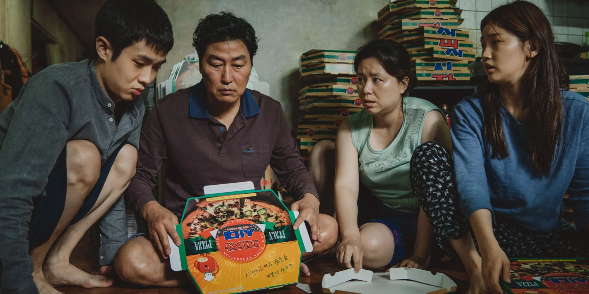 une famille est assise par terre et regarde une boîte en carton de pizza dans Parasite