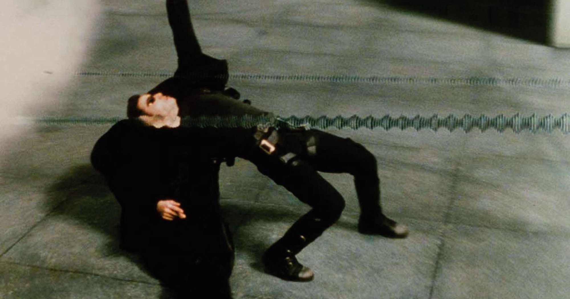 'The Matrix' Keanu Reeves dans le rôle de Neo esquivant en arrière vêtu de noir, alors que les balles volent.