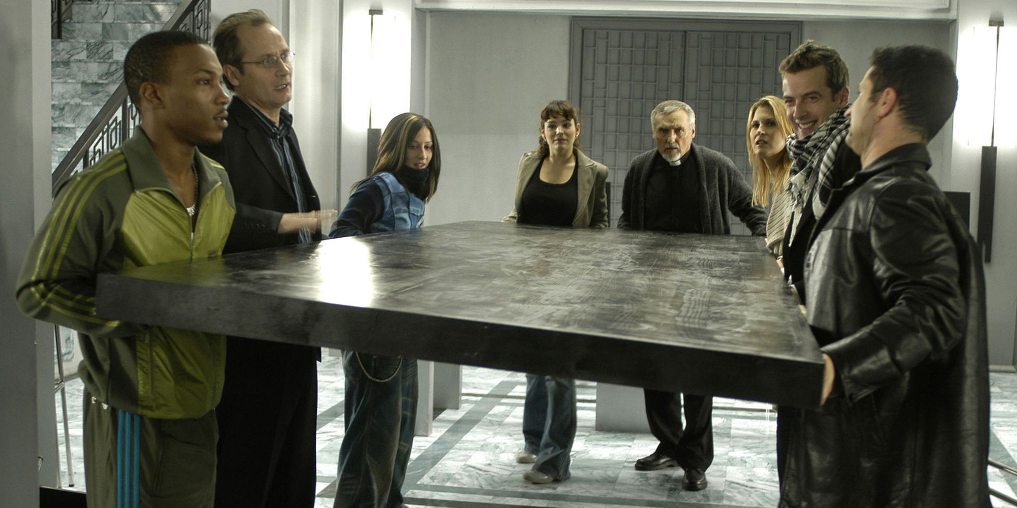 Un groupe de personnes, dont Dennis Hopper, Kelly Brook et Peter Capaldi, portant une table dans House of 9