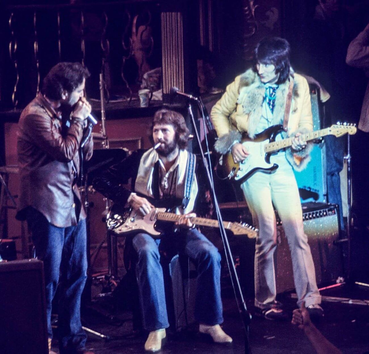 Paul Butterfield tient un micro à côté d'Eric Clapton et Ronnie Wood, qui jouent de la guitare.