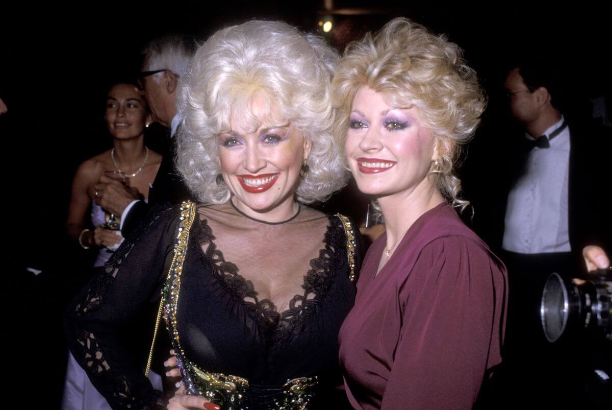 Dolly Parton porte du noir et se tient aux côtés de sa sœur Rachel, qui porte du violet.