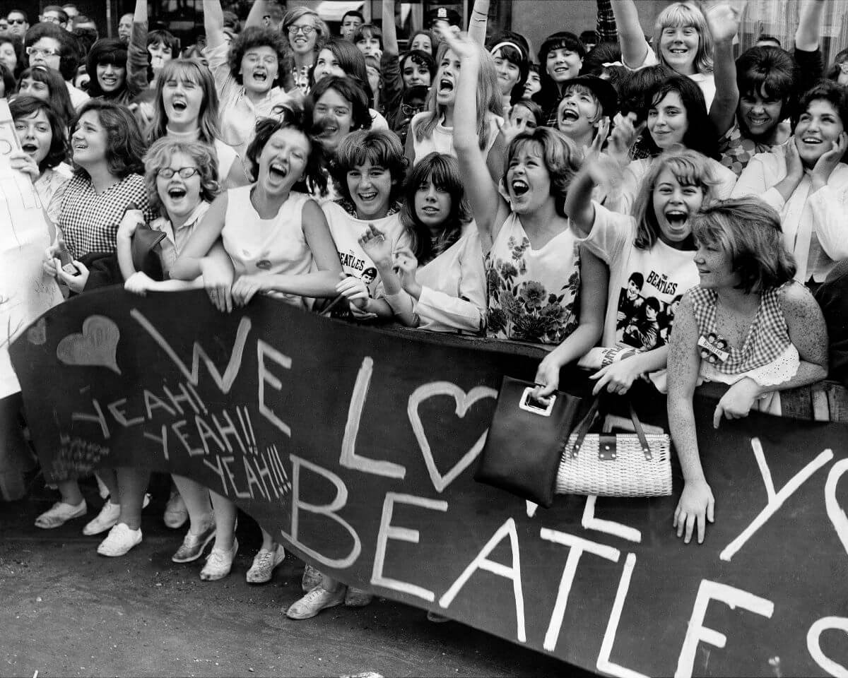 Un groupe de fans des Beatles se tient derrière une banderole qui dit "Nous vous aimons les Beatles."