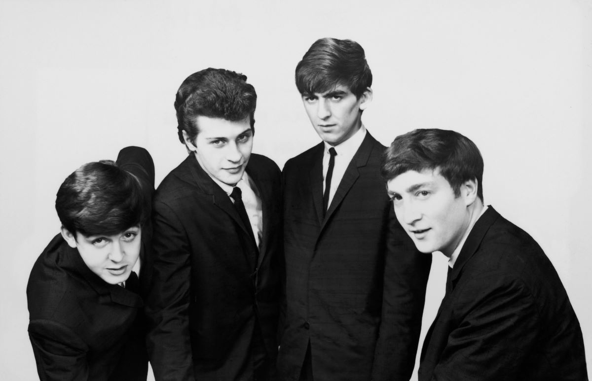 Une photo en noir et blanc de Paul McCartney, Pete Best, George Harrison et John Lennon portant des costumes.