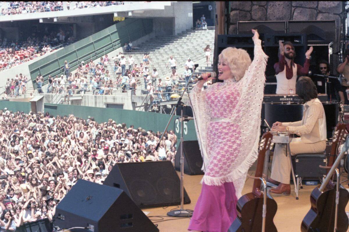 Dolly Parton chante dans un micro sur scène devant un large public.