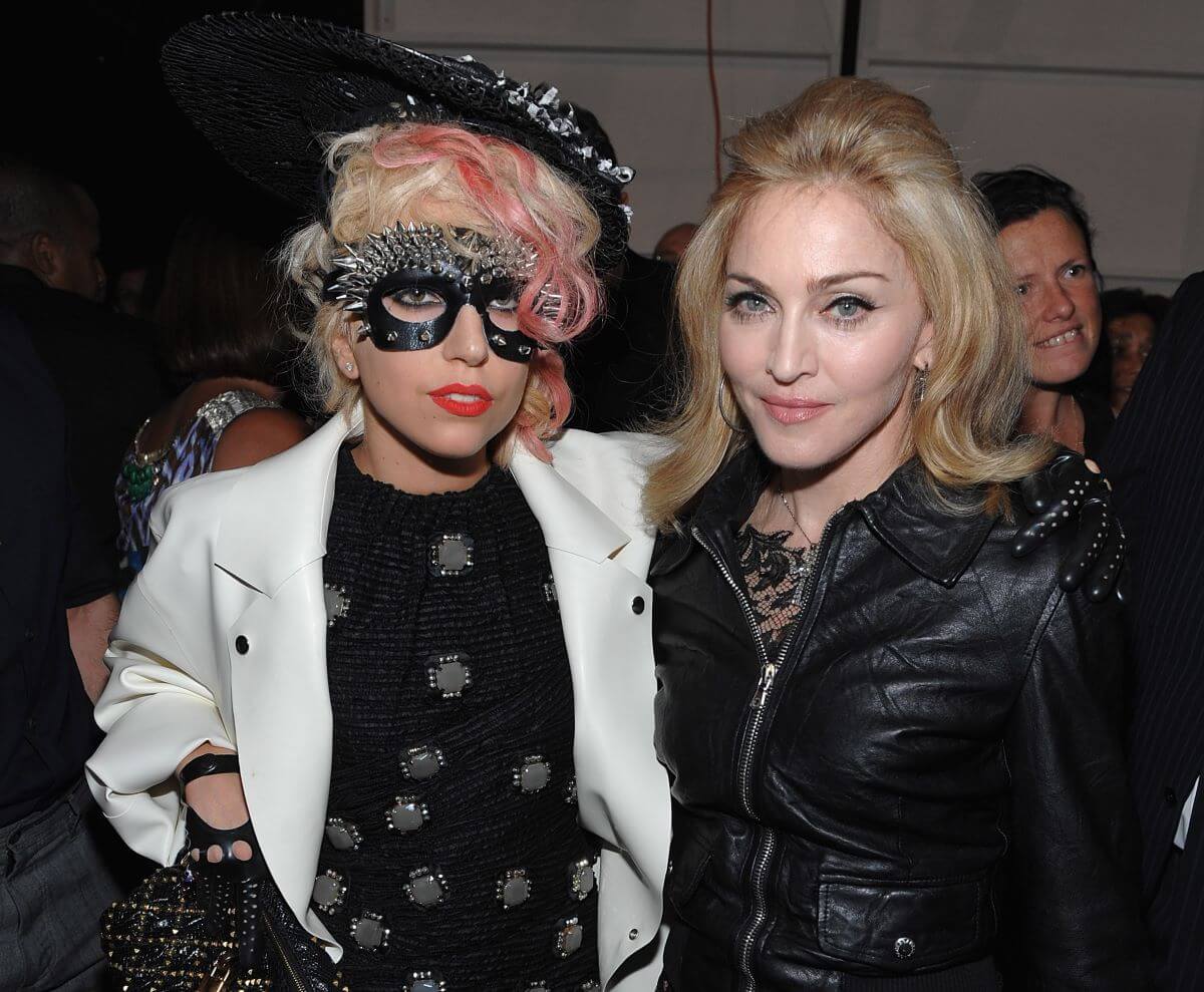 Lady Gaga porte un masque pour les yeux et un chapeau cloutés. Elle se tient aux côtés de Madonna, qui porte du noir.