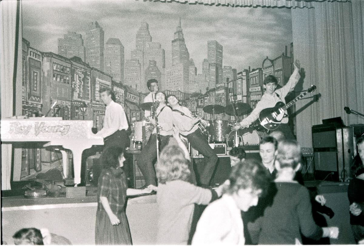 Une photo en noir et blanc des Beatles se produisant sur scène à Hambourg pendant que leur public danse.