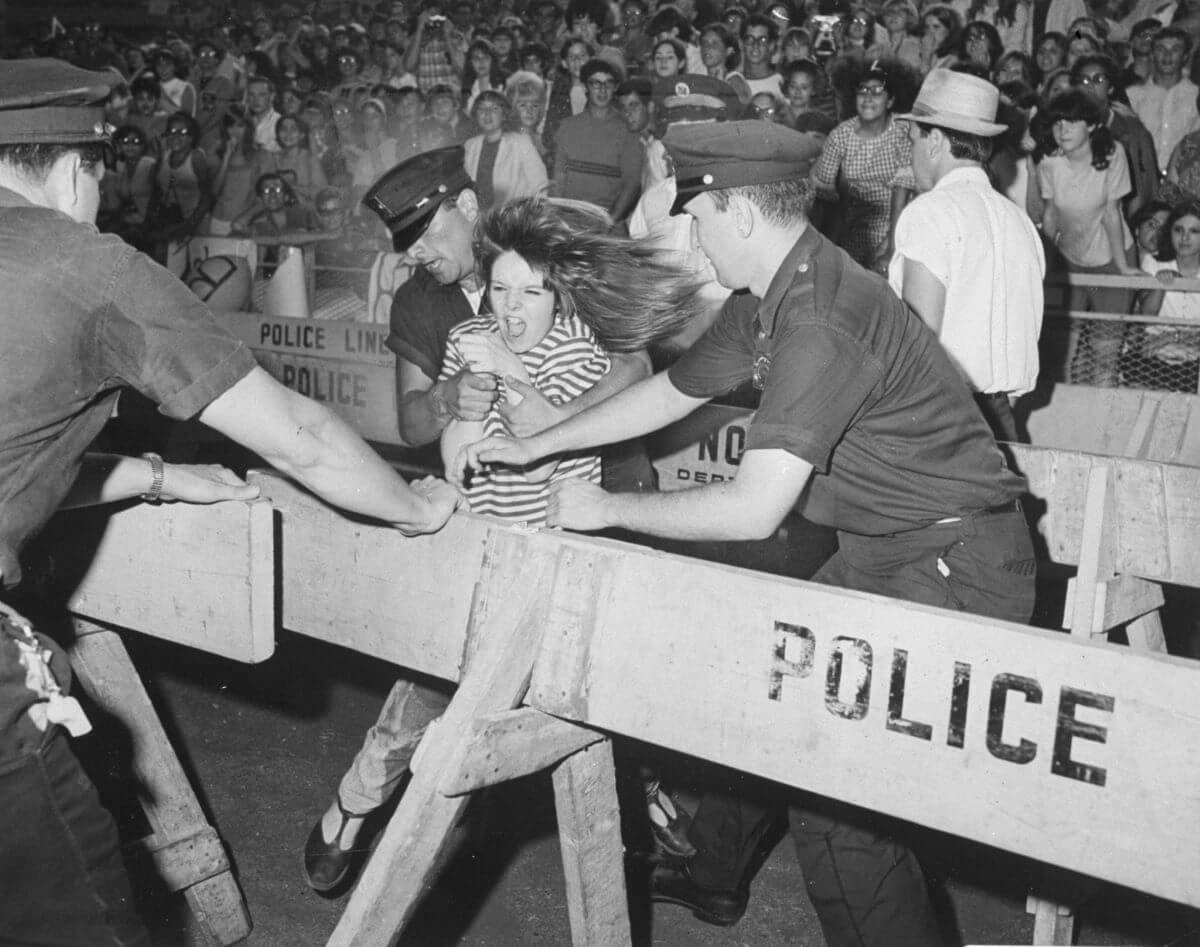Une photo en noir et blanc de policiers arrêtant un fan des Beatles qui se précipite.