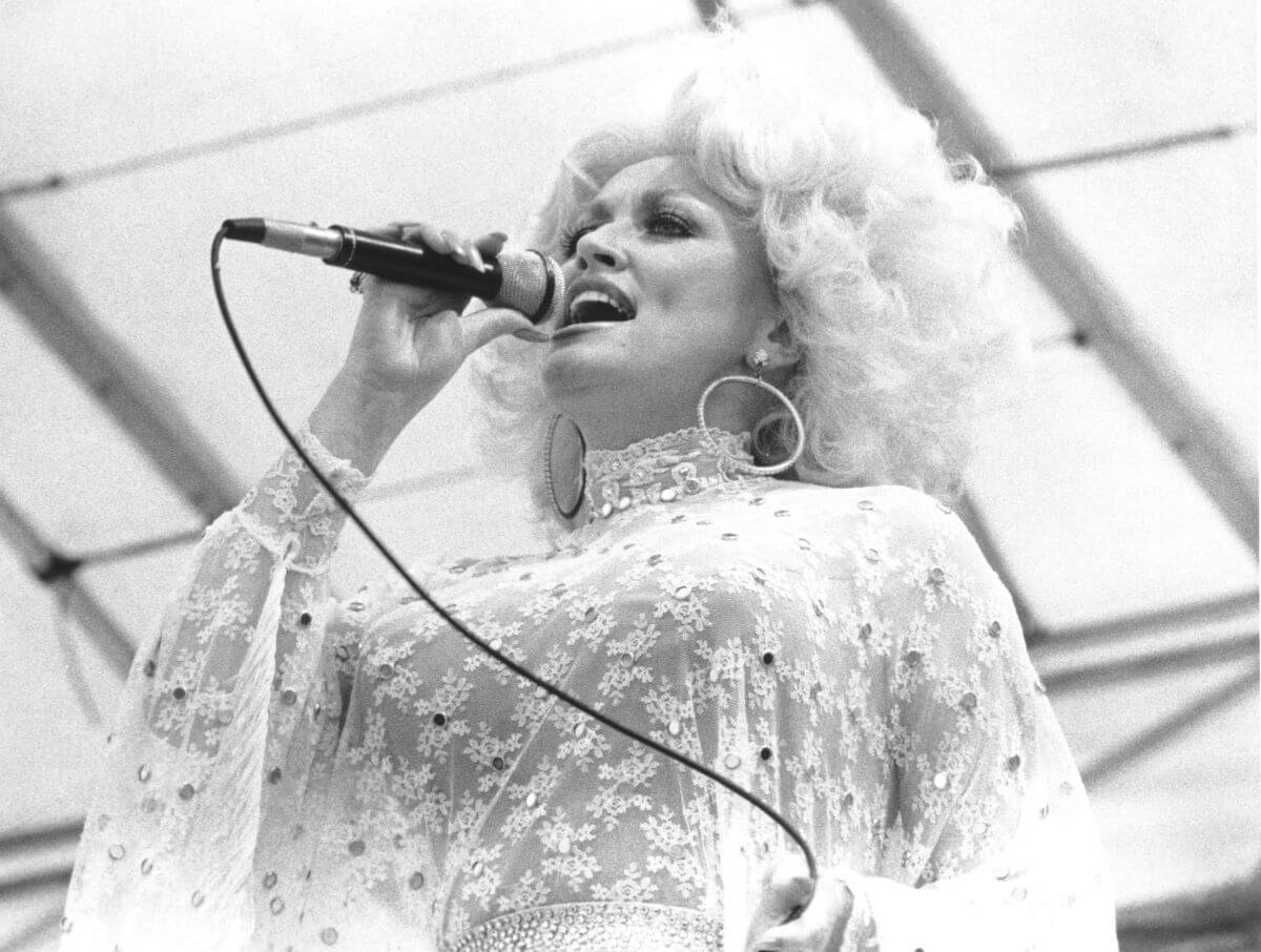 Une photo en noir et blanc de Dolly Parton portant de la dentelle et chantant dans un microphone.