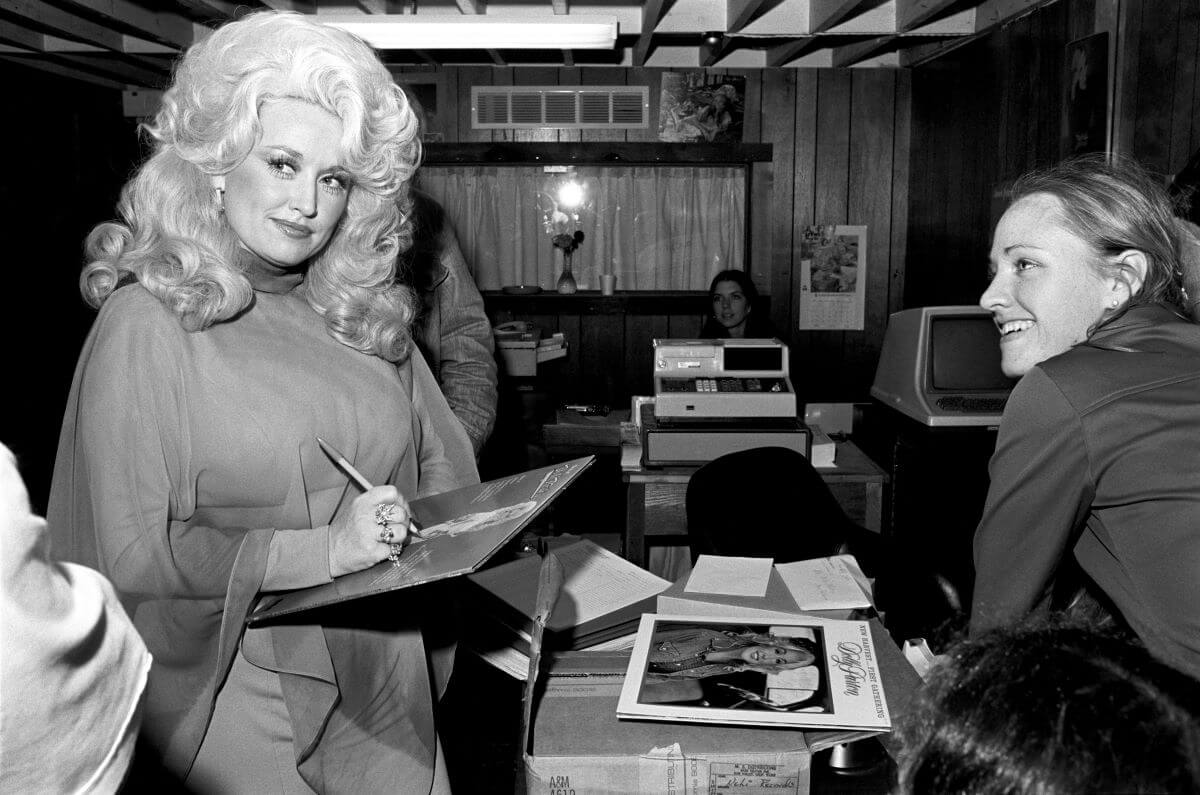 Une photo en noir et blanc de Dolly Parton debout devant un comptoir devant une femme et signant un disque.
