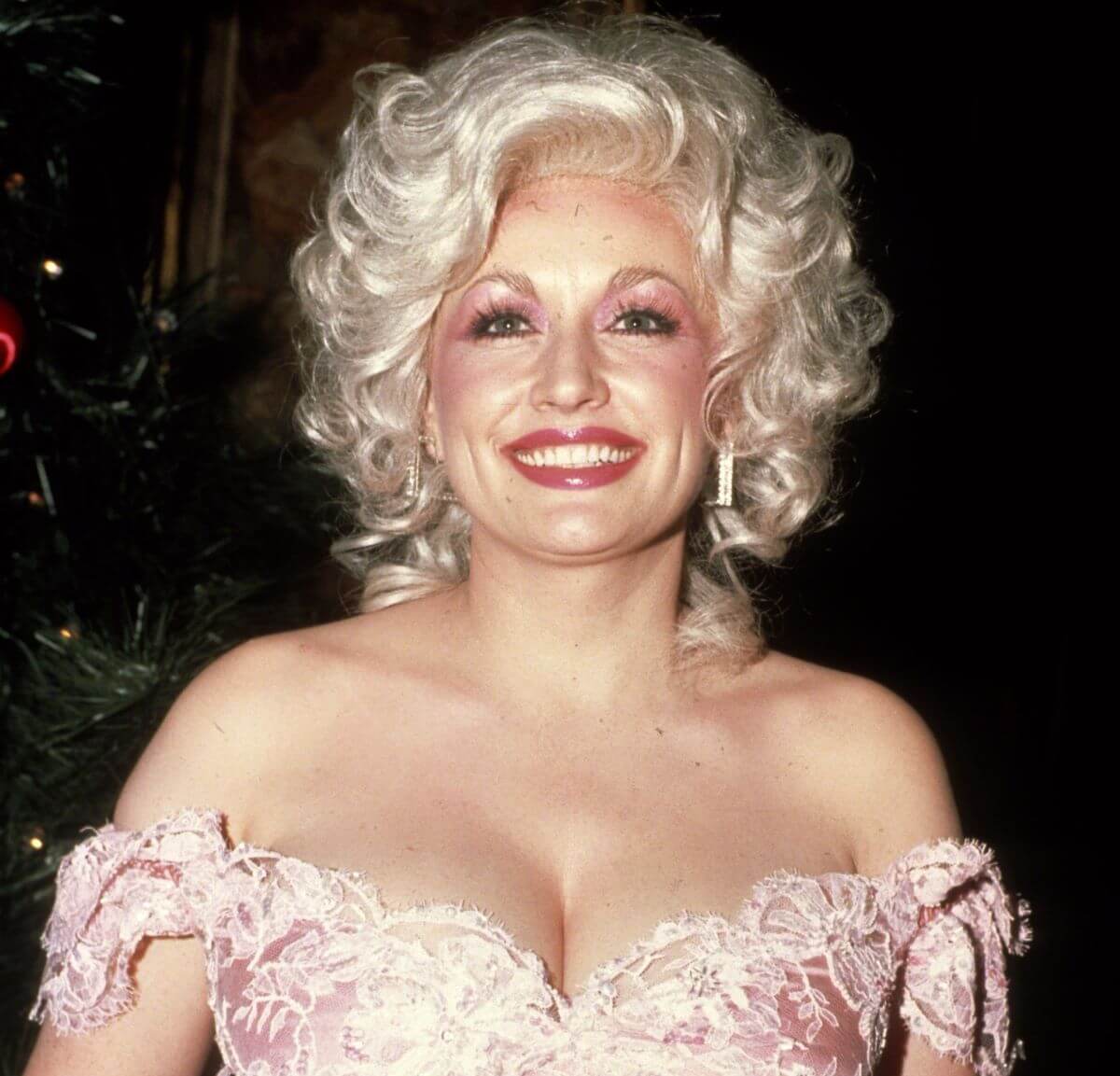 Dolly Parton porte une robe rose. Elle sourit.