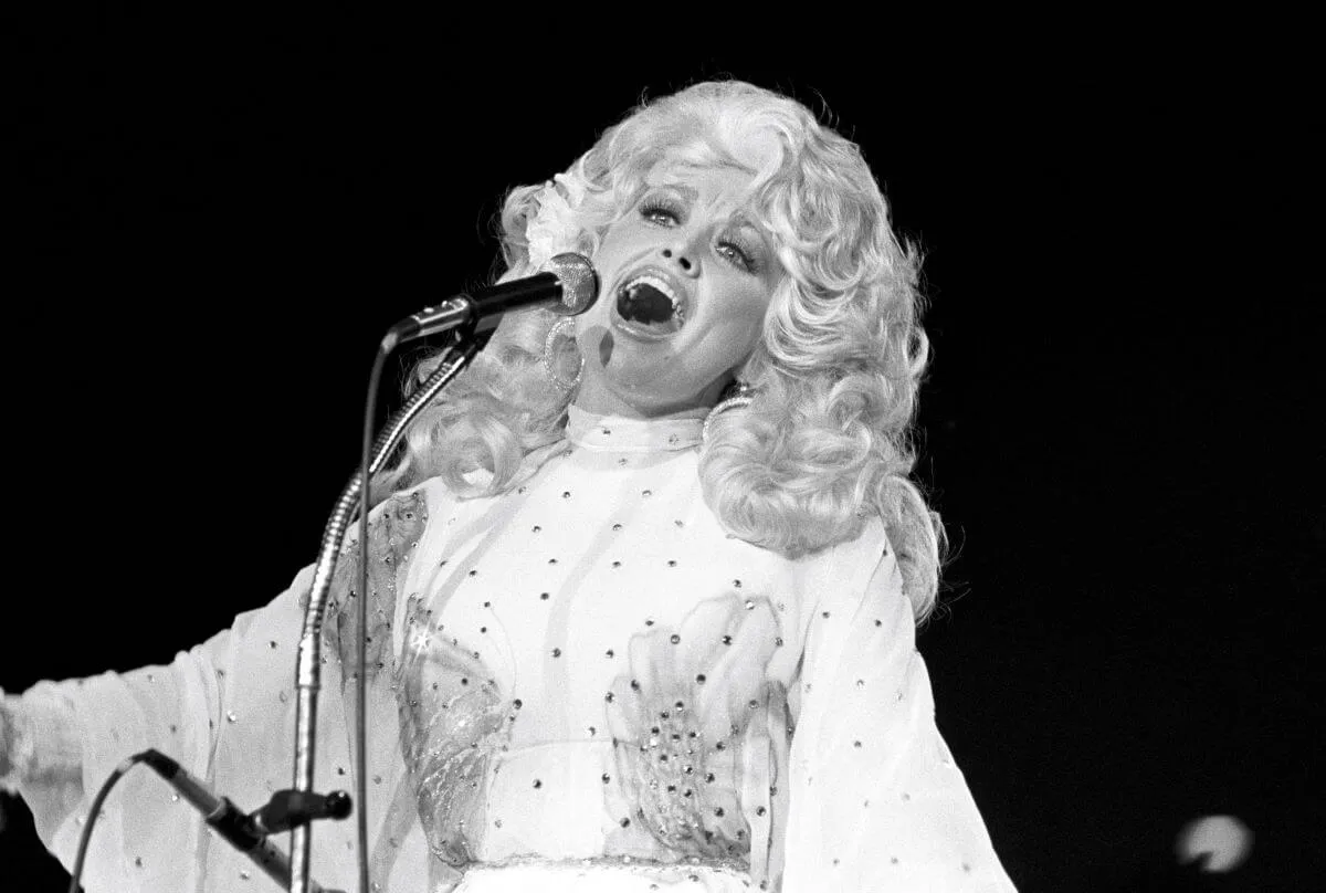 Une photo en noir et blanc de Dolly Parton chantant dans un microphone.
