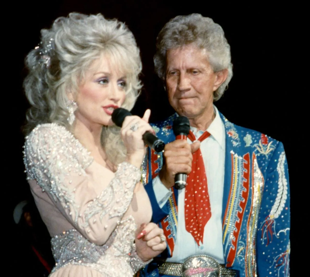 Dolly Parton porte une robe blanche et parle dans un microphone.  Porter Wagoner porte un costume bleu et tient un microphone.